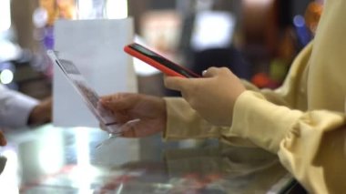 Cep telefonu kullanan üst düzey bir Asyalı Müslüman kadın. NFC kimlik doğrulama ve kimlik doğrulama ödemesi ile birlikte bir satış terminalinde ürün almak için ukalalık yapıyor. 