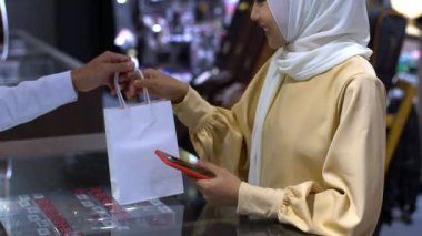 Cep telefonu kullanan üst düzey bir Asyalı Müslüman kadın. NFC kimlik doğrulama ve kimlik doğrulama ödemesi ile birlikte bir satış terminalinde ürün almak için ukalalık yapıyor. 