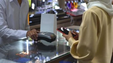 Cep telefonu kullanan üst düzey bir Asyalı Müslüman kadın. NFC kimlik doğrulama ve kimlik doğrulama ödemesi ile birlikte bir satış terminalinde ürün almak için ukalalık yapıyor. 