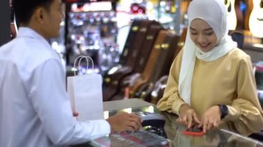 Cep telefonu kullanan üst düzey bir Asyalı Müslüman kadın. NFC kimlik doğrulama ve kimlik doğrulama ödemesi ile birlikte bir satış terminalinde ürün almak için ukalalık yapıyor. 