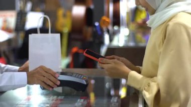 Cep telefonu kullanan üst düzey bir Asyalı Müslüman kadın. NFC kimlik doğrulama ve kimlik doğrulama ödemesi ile birlikte bir satış terminalinde ürün almak için ukalalık yapıyor. 