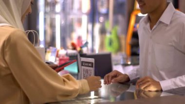 Cep telefonu kullanan üst düzey bir Asyalı Müslüman kadın. NFC kimlik doğrulama ve kimlik doğrulama ödemesi ile birlikte bir satış terminalinde ürün almak için ukalalık yapıyor. 