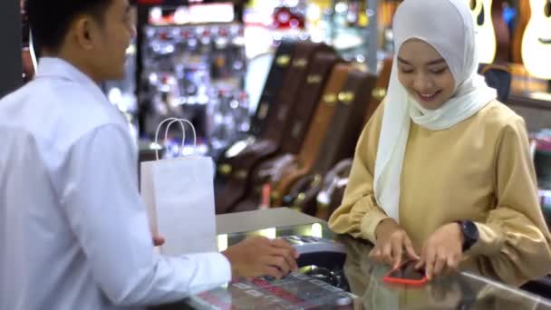 携帯電話を使用して上向きにモバイルアジアのムスリム女性 スマートウォッチは 検証と認証のためのNfc識別支払いで販売端末で製品の支払いをする — ストック動画