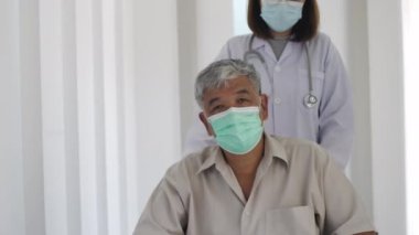Asyalı bir kadın doktor, hastane koridorunda ilerleyen tekerlekli sandalyesinde omurilik fıtığı yüzünden sırt ağrısı çeken yaşlı bir adamı itiyor.