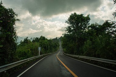 Nan Eyaleti 'ndeki Doi Phuka Ulusal Parkı' nda şafak vakti masmavi gökyüzünün altında yemyeşil ormanlarla çevrili sakin bir dağ manzarasının içinden kırsal bir yol esiyor.