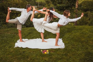 Baba, anne ve kızın ailesi yoga yapıyor. Doğada bir savaşçı figürü.