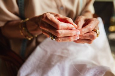 Yaşlı bir kadının dikiş dikmek için iğne ipliği tutan ellerinin ayrıntıları..