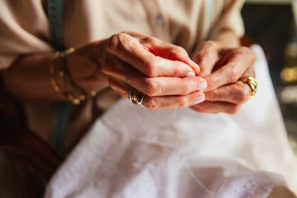 Detail of an older woman's hands threading a needle for sewing.