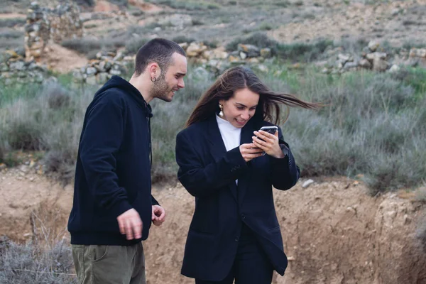 Kız ve oğlan telefona dikkatle gülümseyip doğadaki bir mesajı kontrol ediyorlar.