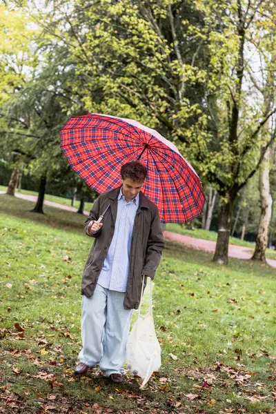 Young boy walking in the park collecting plastics on a rainy day, vertical photo