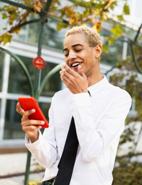 Güzel genç adam gülümsüyor ve mutlu bir şekilde parktaki cep telefonuyla iletişim kuruyor.