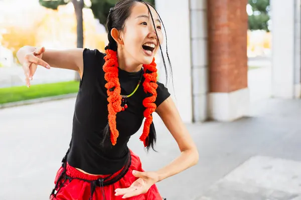 Portrait of Asian woman with an original hairstyle smiling while dancing an urban dance in the street.