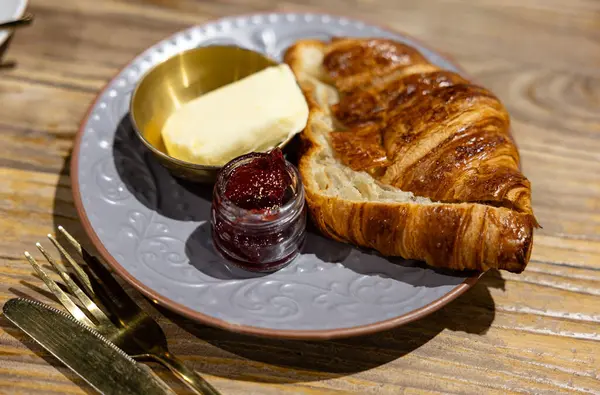 在一个时髦的灰色盘子里放满了丰富的黄油和草莓果酱 随时可以吃早餐的发亮的羊角面包 — 图库照片