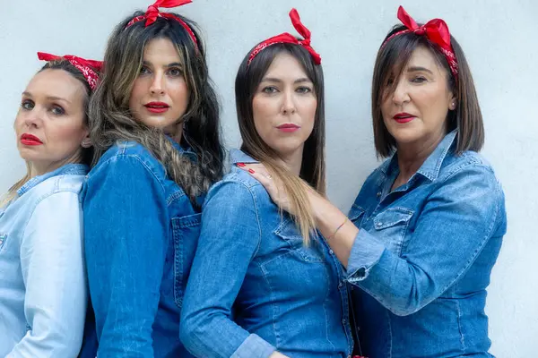 Four determined women wearing denim with red headbands link together, showcasing their bond and collective confidence.