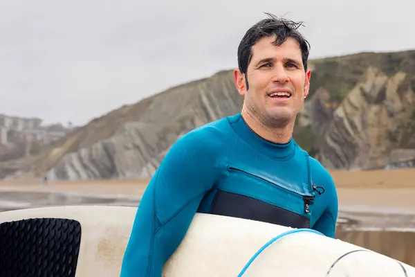 Cheerful Man Teal Wetsuit Holding Surfboard Beach Striking Cliffs Him — Stock Photo, Image