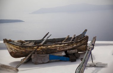 Birçok yolculuğun işaretlerini taşıyan eski ahşap bir tekne Santorini 'deki bir çatıdan Ege Denizi' ne bakıyor..