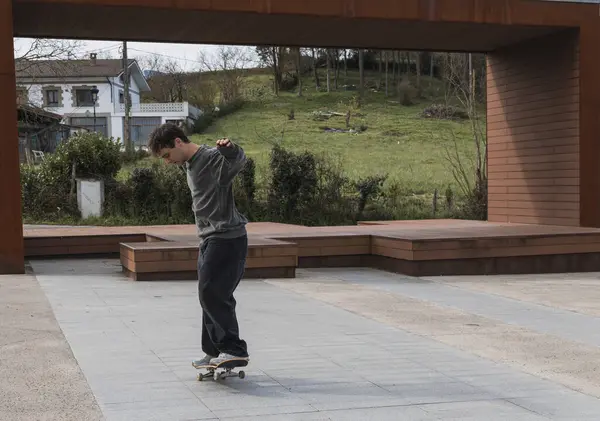スケーターは 緑と都市デザインの背景で 公共のスケートエリアで彼のスキルを示して 中間トリックに捕らえられています — ストック写真