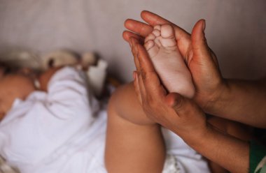 Bir annenin bebeğinin ayağını nazikçe elinde tutmasını gösteren yakın plan görüntüler. Bakımı ve korumayı simgeliyor..