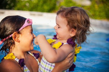 İki genç kız kardeş güneşli bir yaz öğleden sonrasında yüzme havuzunda gülüp oynuyorlar..