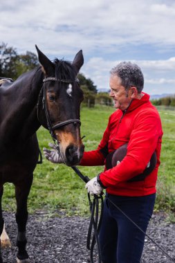 Emekli adam kırsalda atını nazikçe okşuyor, arkadaşlığın ve barışçıl açık hava ortamının tadını çıkarıyor..