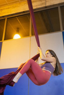 Spor salonundaki bordo kumaşı sıkıca tutan bir kadın akrobatik bir performansa hazırlanıyor.. 