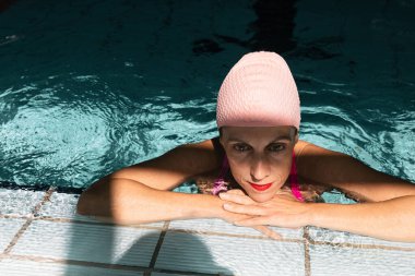 Kapalı bir yüzme havuzunun kenarında dinlenen pembe yüzme şapkası takan, yüzdükten sonra mola veren sağlıklı bir kadın..