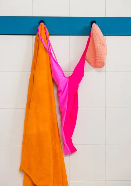 stock image Photograph of a brightly colored pink swimsuit, orange towel, and peach swim cap hanging in an indoor pool locker room, ready for swimming.