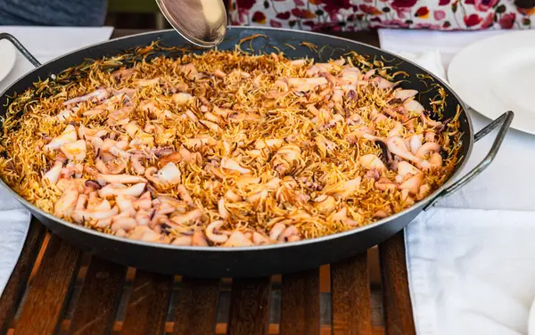 stock image A large pan of traditional seafood noodle is presented on a wooden dining table.