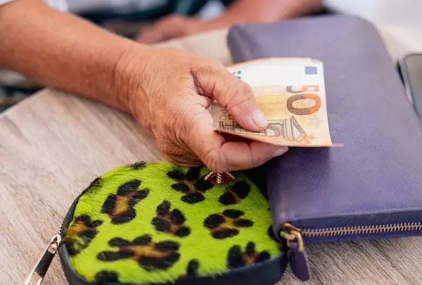 Kafe masasındaki cüzdanın yanında 50 Euro 'luk banknot tutan bir el resmi..