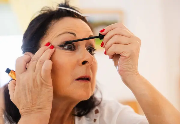 Yaşlı kadın makyaj için rimel sürüyor.