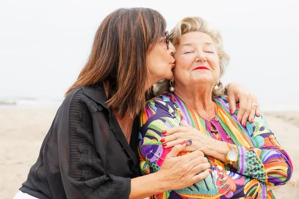 Yetişkin kız sahilde yaşlı anneyi öpüyor.