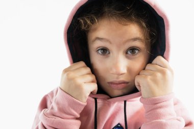 Ciddi ve odaklanmış bir ifadeyle pembe kapüşonlu genç bir kız kapüşonunu sıkıca yüzüne tutuyor..