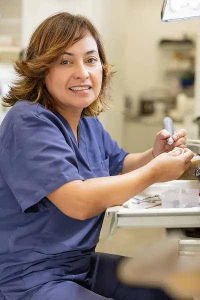Profesyonel bir laboratuvarda protez üzerinde çalışırken elinde diş aleti tutan gülümseyen bir diş teknisyeni.