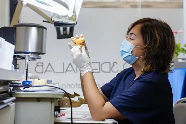 Diş teknisyeni eldiven ve maske takıyor ve protez bir model üzerinde çalışıyor..