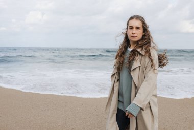 Yağmurluk giymiş genç bir kadın dalgalardan kaçmak için sahil boyunca koşuyor..