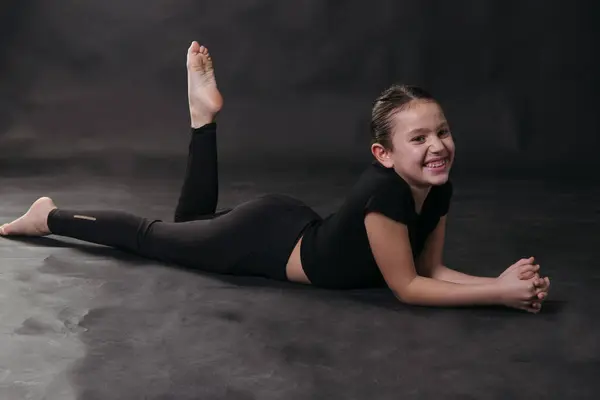 Spor kıyafetli genç bir kızın portresi. Stüdyonun zemininde siyah bir zeminde yatarken gülümsüyor..