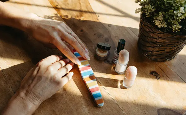 Manikür seansı, çivi bakım ürünleriyle birlikte, doğal ışıkta, ahşap bir masada.