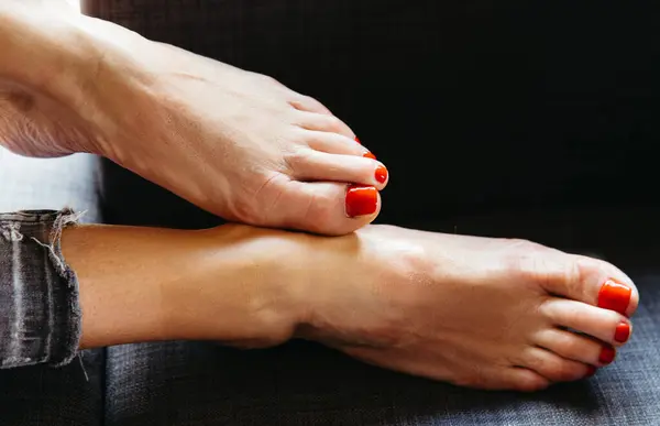 Kırmızı tırnaklı kadın ayaklarının yakın çekimi, arka planda kapalı alanda dinleniyor..