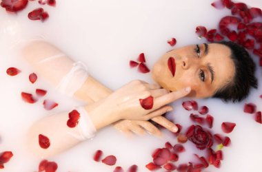 Süt banyosunda yaprakları ve sakin ifadesiyle dinlenen zarif bir kadın.