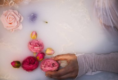 Sütlü banyoda pembe güller ve ince dantelli bir kadın eli.