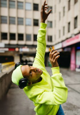 Neon kıyafetli genç adam şehir sokağında gökyüzüne telefon kaldırıyor.