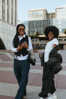 İki şık siyahi arkadaş gülümsüyor ve şehirde kameraya bakıyor.