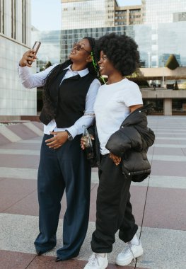 Şehirde gülümseyen ve selfie çeken iki genç siyahi kadın.