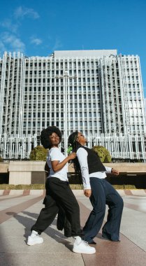 İki siyah arkadaş uzun şehir binaları arasında dans ediyor.