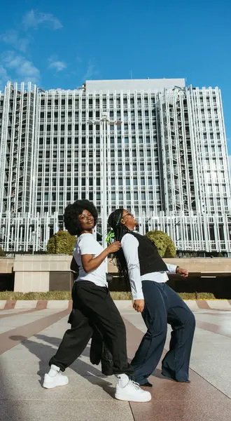 İki siyah arkadaş uzun şehir binaları arasında dans ediyor.