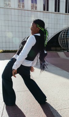 Afro genç modern şehir binaları arasında dans pozu veriyor.