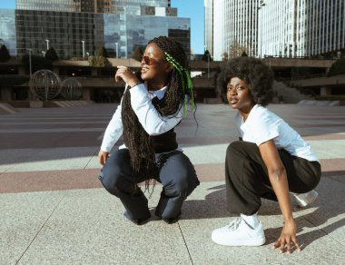 Şehir caddesinde dans hareketleri arasında dinlenen genç Afro kadınlar