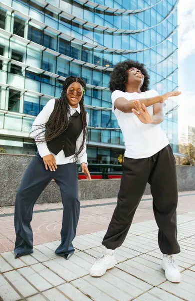 İki genç siyah kadın şehirde dans ediyor ve gülümsüyor.