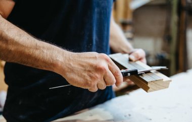 Marangozluk atölyesinde ahşabı ölçmek için kalibre kullanan adam, yakın plan.