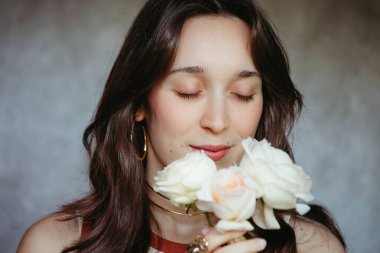 Beyaz güllerin kokusundan zevk alan sakin bir kadının portresi.